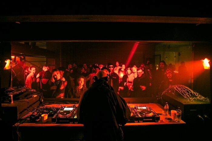 DJ performs electronic music before a crowd in a red-lit club