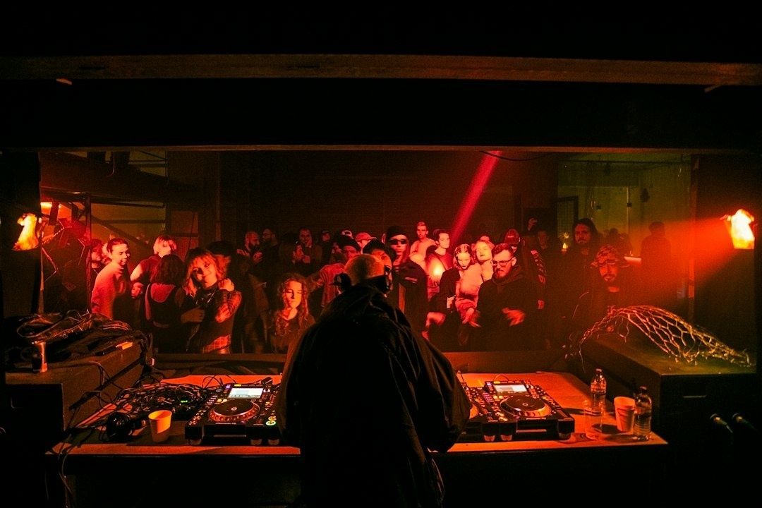 DJ performs electronic music before a crowd in a red-lit club