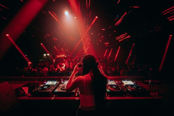 DJ at a booth faces a crowd under intense red club lighting