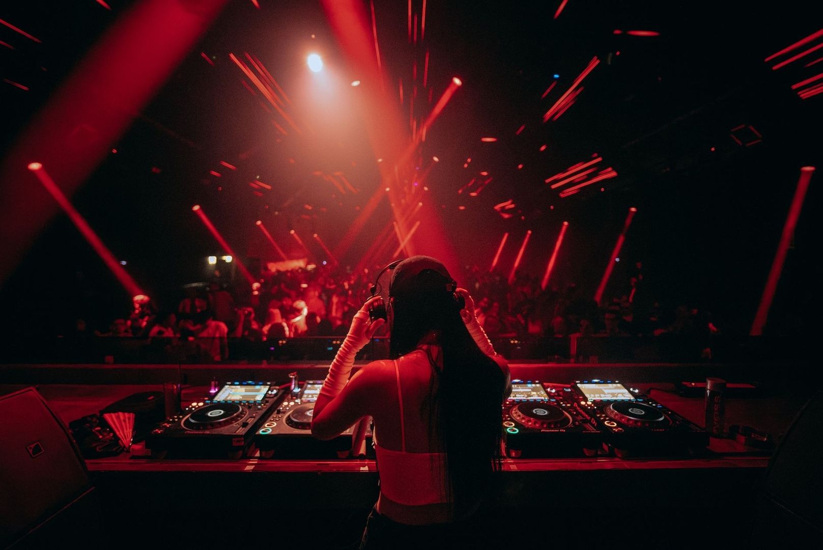 DJ at a booth faces a crowd under intense red club lighting