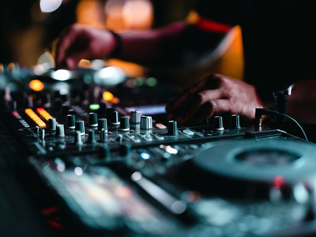 DJ adjusting controls on a mixer beside a turntable in dim light
