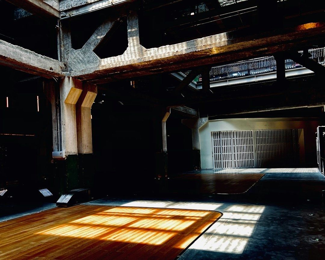 Sunlit industrial concrete interior with a wooden floor and barred entrance