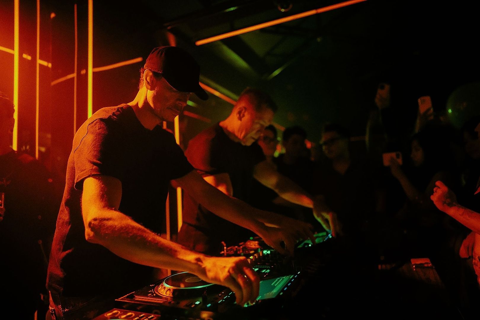 DJ performing in a dark club with warm orange and green lighting