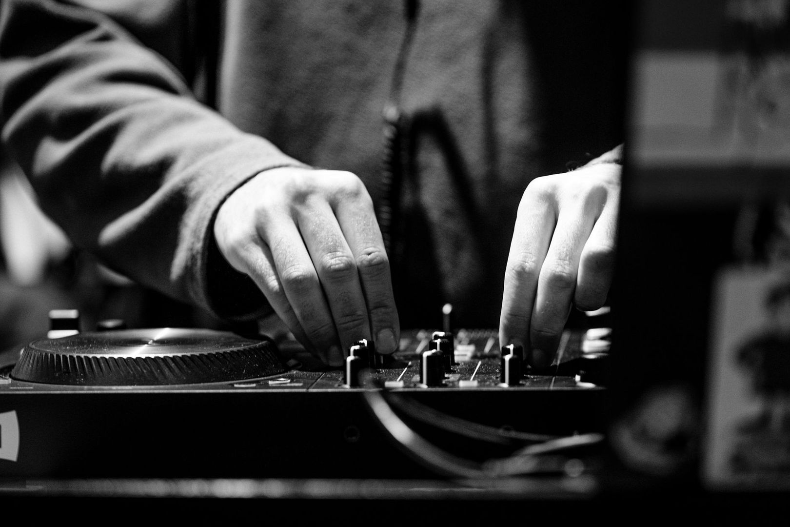 DJ adjusting knobs on a turntable and analog mixer in monochrome
